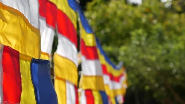 Banderas de oración budistas balanceándose en el viento en los rayos del sol naciente en un templo. Primer plano de grabación en cámara lenta. Profundidad superficial del campo — Vídeo de stock