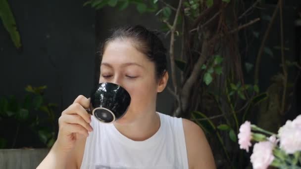 Hermosa joven feliz bebe café en la cafetería por la mañana. modelo femenino disfrutando de café expreso o té . — Vídeos de Stock