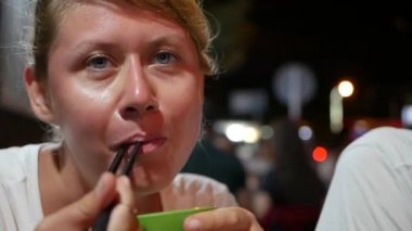 Asya gece sokak gıda pazarında yemek çubukları ile balık ve pirinç erişte yeme Kadın. Yakın çekim