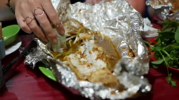 Los turistas comen rollos de primavera con pescado cocinado en papel de aluminio en el mercado asiático de alimentos callejeros. De cerca. — Vídeo de stock