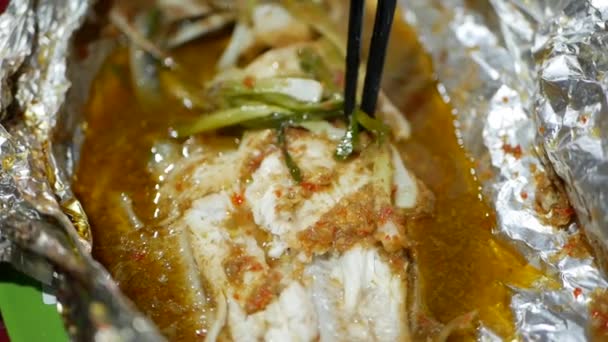 Touristen essen auf einem asiatischen Street-Food-Markt Fisch mit Stäbchen in Folie gekocht. Nahaufnahme — Stockvideo