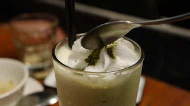 Cam bardak krem şanti ile lezzetli matcha çay frappe. Kız matcha buzlu çay ile cam bir kaşık ile krem yiyor. Closeup