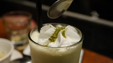 Cam bardak krem şanti ile lezzetli matcha çay frappe. Kız matcha buzlu çay ile cam bir kaşık ile krem yiyor. Closeup