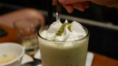 Cam bardak krem şanti ile lezzetli matcha çay frappe. Kız matcha buzlu çay ile cam bir kaşık ile krem yiyor. Closeup