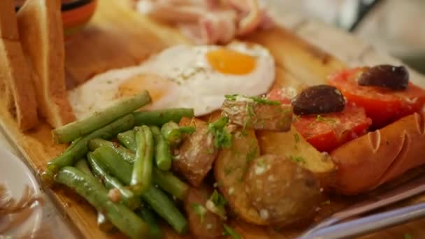 Förflyttning av traditionell engelsk frukost med stekt ägg, korv, gröna bönor, potatis, champinjoner, tomater, rostat bröd, skinka och bacon på en trä skiva. Närbild — Stockvideo