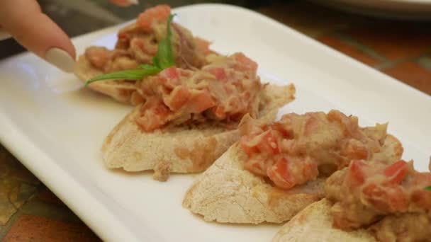 Die weibliche Hand nimmt Bruschetta mit Avocado und Tomate von einem Teller in einem Restaurant. Nahaufnahme — Stockvideo