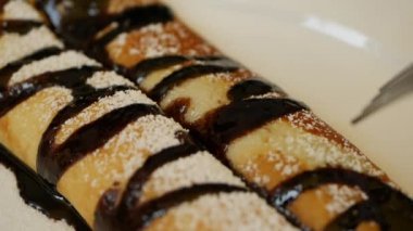 Çatal ve bıçak kullanan müşteri taze mango, çikolata ve pudra şekerli lezzetli krepler yiyor. Restoranda beyaz tabağa konmuş. Yakın plan.