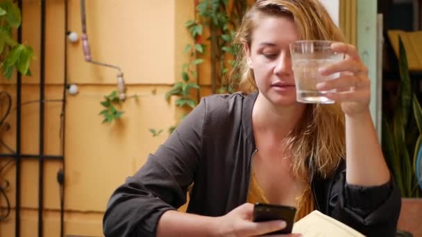 Happy girl utilise un smartphone, écrit un message, bavarde. Jeune femme cherchant des informations au téléphone. Assis au restaurant avec des amis. Heure du petit déjeuner — Video