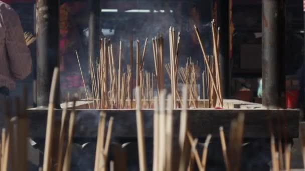 People praying and worshipping in Taoist temple interior bowing and holding incense sticks during the celebration of Chinese New Year. The big outdoor pot with incenses, fulfilled with sand, is — Stock Video