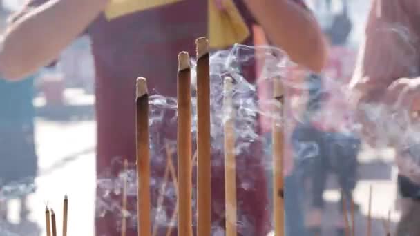 Люди молятся и поклоняются в даосском храме, кланяясь и держа в руках благовонные палочки во время празднования китайского Нового года. Большой открытый горшок с зажигалками, наполненный песком, — стоковое видео