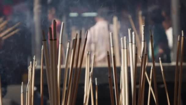 People praying and worshipping in Taoist temple interior bowing and holding incense sticks during the celebration of Chinese New Year. The big outdoor pot with incenses, fulfilled with sand, is — Stock Video