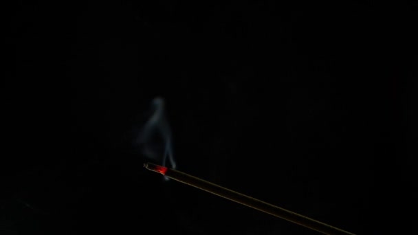 Detailní pohled na hořící vonnou tyčinku. Kouř fouká z konce žhavého září. Vůně uvolněná z kadidla na černém pozadí. Relaxace, meditace a aromaterapie — Stock video