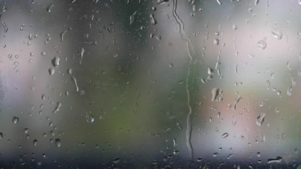 El agua de lluvia fuerte se descarga contra el vidrio de la ventana y fluye hacia abajo. Primer plano. Gotas de lluvia sobre fondo de vidrio en temporada de lluvias — Vídeos de Stock