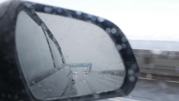 View out the rear view mirror as car drives on highway in the rain — Stock Video