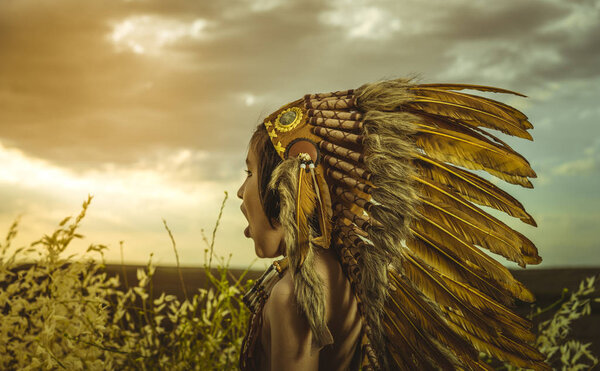 American Indian boy dressed in traditional feathered costume, wearing a tuft on his head, picture at sunset in a wheat field