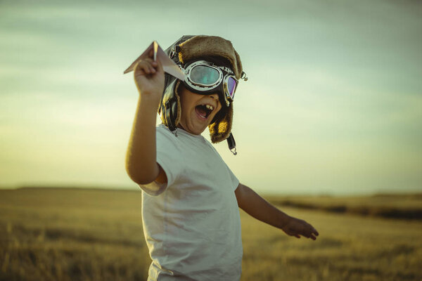 Happy boy at sunset playing at being aviator, he wears pilot glasses of airplanes and some cardboard like wings