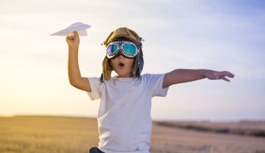 Küçük çocuk kask ve günbatımında bir kağıt uçak oynarken bir pilot olma hayalleri