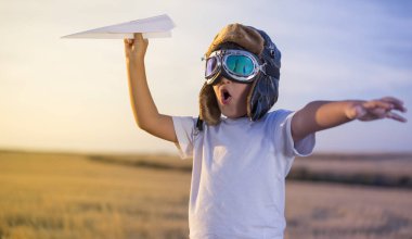 Eğlenceli küçük çocuk kask ve günbatımında bir kağıt uçak oynarken bir pilot olma hayalleri