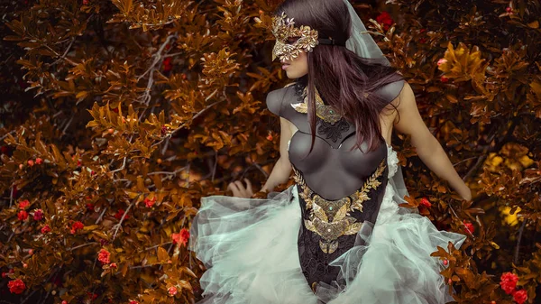 秋の庭で銅と金の色の葉のマスクをした白い服を着た謎の女性 — ストック写真