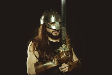 İskandinav, metalik miğferli ve hayvan derili Viking savaşçısı. deri eldivenler, altın süslemeleri ve çelik kılıç ile kırmızı ahşap kalkan