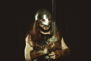 Metalik miğferli ve hayvan derili Viking savaşçısı. deri eldivenler, altın süslemeleri ve çelik kılıç ile kırmızı ahşap kalkan