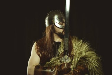 Metalik miğferli ve hayvan derili Viking savaşçısı. deri eldivenler, altın süslemeleri ve çelik kılıç ile kırmızı ahşap kalkan