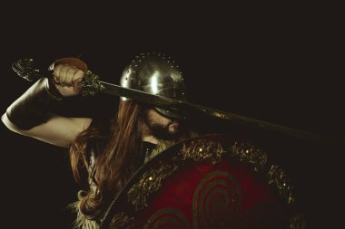 Metalik miğferli ve hayvan derili Viking savaşçısı. deri eldivenler, altın süslemeleri ve çelik kılıç ile kırmızı ahşap kalkan