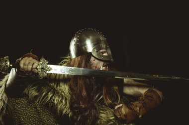 Metalik miğferli ve hayvan derili Viking savaşçısı. deri eldivenler, altın süslemeleri ve çelik kılıç ile kırmızı ahşap kalkan