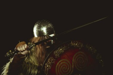 İskandinav, metalik miğferli ve hayvan derili Viking savaşçısı. deri eldivenler, altın süslemeleri ve çelik kılıç ile kırmızı ahşap kalkan