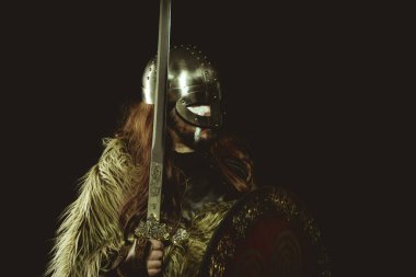 Metalik miğferli ve hayvan derili Viking savaşçısı. deri eldivenler, altın süslemeleri ve çelik kılıç ile kırmızı ahşap kalkan