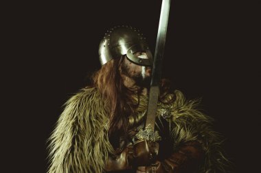 Metalik miğferli ve hayvan derili Viking savaşçısı. deri eldivenler, altın süslemeleri ve çelik kılıç ile kırmızı ahşap kalkan