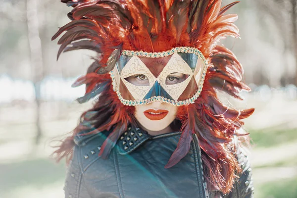 redhead woman with Venetian style mask with red feathers and gold pieces.