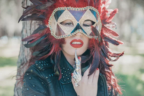 carnival, redhead woman with Venetian style mask with red feathers and gold pieces.