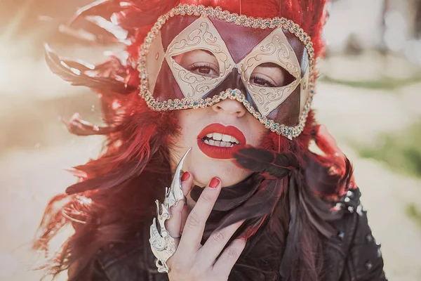 redhead woman with Venetian style mask with red feathers and gold pieces.
