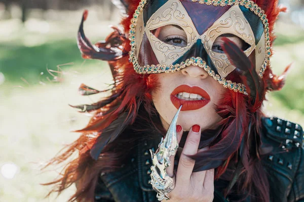 Glamour, redhead woman with Venetian style mask with red feathers and gold pieces.