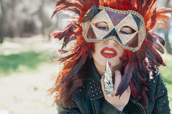 redhead woman with Venetian style mask with red feathers and gold pieces.