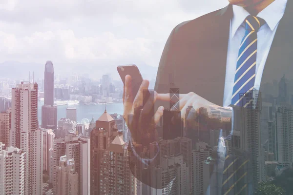 Double exposure businessman hand holding and touch screen smart phone with modern city background. Mobile, Urban, City of business, Telecommunication and Technology concept. With copy space.