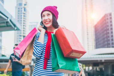Birçok alışveriş torbaları ve gülümseme tutan bir heyecanlı güzel genç kız giyim gömlek ve yün şapka portresi. Kopya alanı ile. Mutlu gülümseyen kadın müşteri. Güzel genç beyaz. yaşam tarzı, iskonto