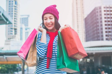 Birçok alışveriş torbaları ve gülümseme tutan bir heyecanlı güzel genç kız giyim gömlek ve yün şapka portresi. Kopya alanı ile. Mutlu gülümseyen kadın müşteri. Güzel genç beyaz. yaşam tarzı, iskonto