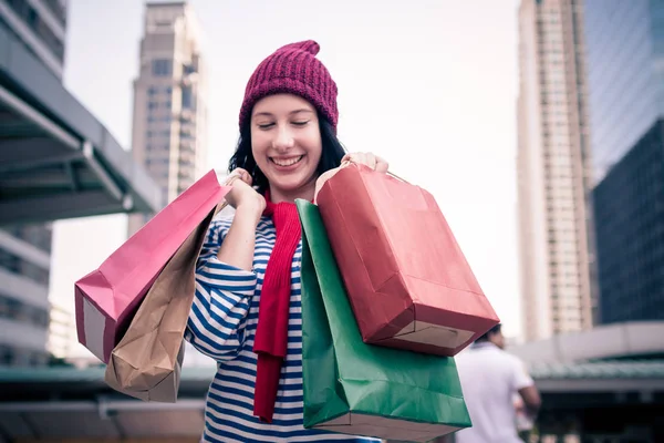 Birçok alışveriş torbaları ve gülümseme tutan bir heyecanlı güzel genç kız giyim gömlek ve yün şapka portresi. Kopya alanı ile. Mutlu gülümseyen kadın müşteri. Güzel genç beyaz. yaşam tarzı, iskonto