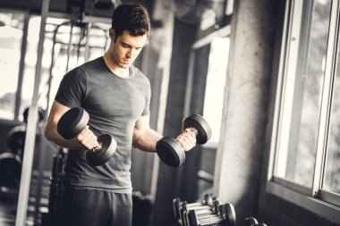 Beyaz yakışıklı genç ve büyük kas spor içinde uygun. Genç adam bir spor salonunda bir egzersiz dersi sırasında dumbbell tutarak. Sağlıklı spor yaşam tarzı, Fitness kavramı.