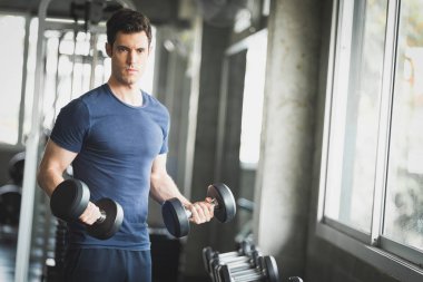 Beyaz yakışıklı genç ve büyük kas spor içinde uygun. Genç adam bir spor salonunda bir egzersiz dersi sırasında dumbbell tutarak. Sağlıklı spor yaşam tarzı, Fitness kavramı.