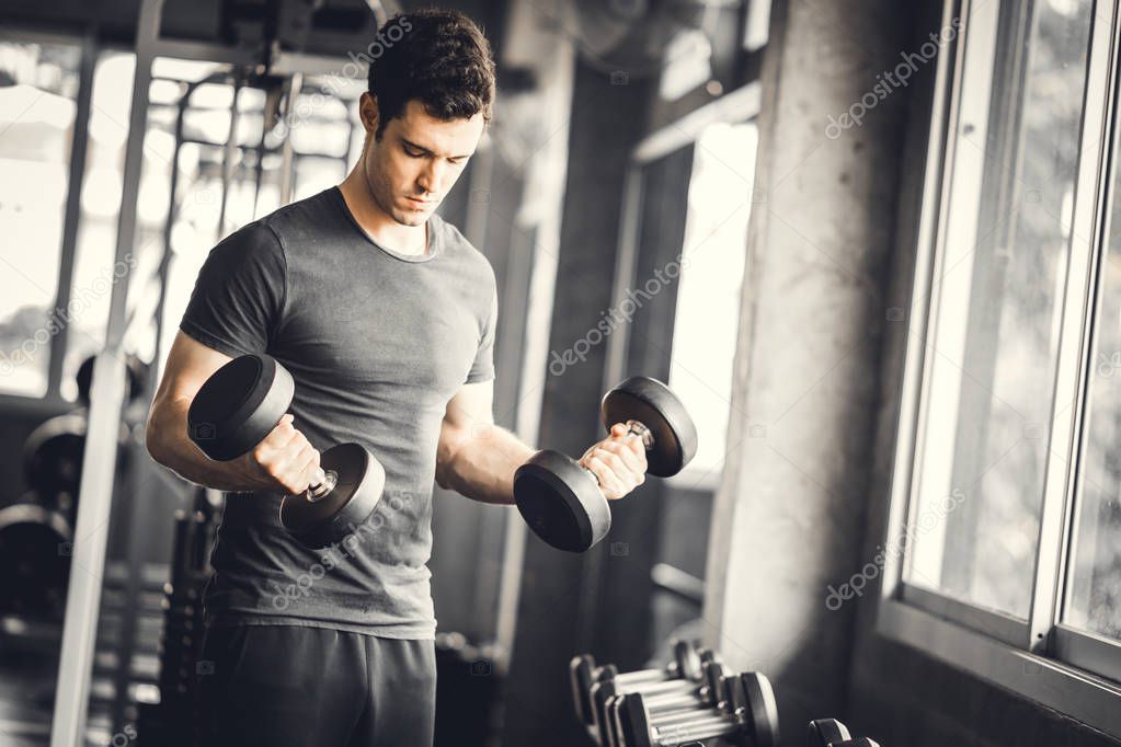 Fit caucasian handsome young man and big muscle in sportswear. Young man holding dumbbell during an exercise class in a gym. Healthy sports lifestyle, Fitness concept.