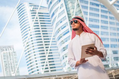 Yakışıklı Arap iş adam tutun dijital tablet ve sol tarafa bakıyor. Dış office ayakta Arap iş adam. Bir buluşma, bağlantı kavramı bitirme. kopya alanı ile