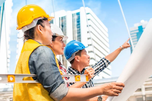 Three industrial engineer wear safety helmet engineering working and talking with drawings inspection on building outside. Engineering tools and construction concept.