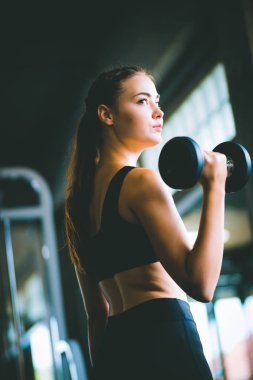 Güzel genç kadın beyaz spor giyim kameraya poz uygun. Bir spor salonunda bir egzersiz dersi sırasında halter tutan genç kadın. Sağlıklı spor yaşam tarzı, Fitness kavramı.