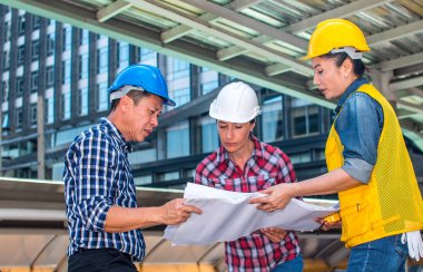 Üç endüstri mühendisi aşınma emniyet kask mühendislik çalışma ve çizimler muayene ile binanın önünde konuşurken. Mühendislik araçları ve inşaat kavramı. Kopya alanı ile