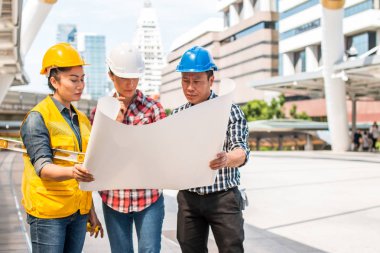 Üç endüstri mühendisi aşınma emniyet kask mühendislik çalışma ve çizimler muayene ile binanın önünde konuşurken. Mühendislik araçları ve inşaat kavramı. Kopya alanı ile