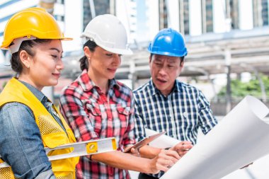 Üç endüstri mühendisi aşınma emniyet kask mühendislik çalışma ve çizimler muayene ile binanın önünde konuşurken. Mühendislik araçları ve inşaat kavramı.
