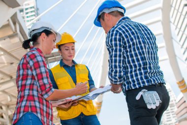 Üç endüstri mühendisi aşınma emniyet kask mühendislik çalışma ve çizimler muayene ile binanın önünde konuşurken. Mühendislik araçları ve inşaat kavramı. Kopya alanı ile